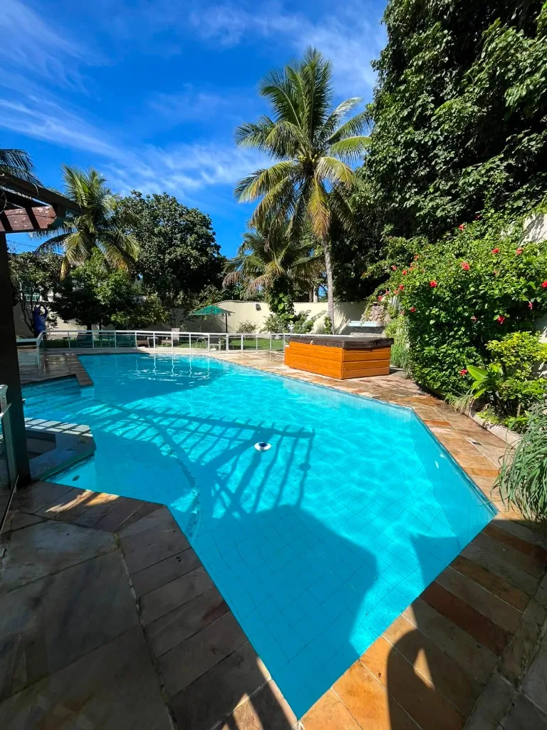 Piscina residencial tropical com água cristalina, palmeiras e deck de pedra